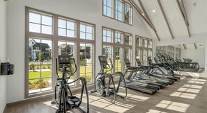 A gym with multiple treadmills and elliptical machines, large windows with a view of a residential area, and a high ceiling with wooden beams. - Landing | Modern 1BD, Courtyard, Gym (Mobile)