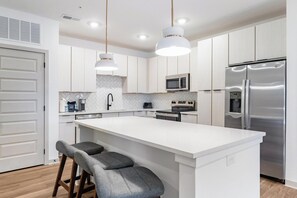 A modern kitchen with white cabinetry, a central island with bar stools, stainless steel appliances, and pendant lighting.