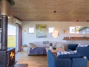 A cozy living room with a wood-burning stove, a sofa, a blue armchair, a dining table, and a large abstract painting on the wall. - 4 Star Holiday Home in Lokken (Lokken)