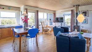 Un'ampia zona giorno con soffitto in legno, una televisione, un camino e un'area pranzo con sedie blu e un tavolo.