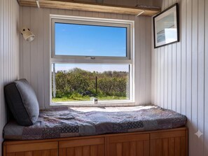 A room with a large window, a bench with a cushion, and a framed picture on the wall. - 4 Star Holiday Home in Lokken (Lokken)