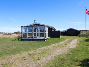A glasshouse structure with a metal roof, surrounded by a grassy field and a gravel path. - 4 Star Holiday Home in Lokken (Lokken)