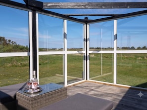 A glass-enclosed outdoor seating area with a view of a grassy field. - 4 Star Holiday Home in Lokken (Lokken)