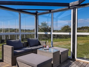 A covered outdoor seating area with a glass enclosure, wicker furniture, and a clear view of the surrounding landscape. - 4 Star Holiday Home in Lokken (Lokken)