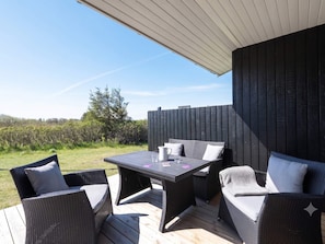 An outdoor patio with wicker furniture and a table, surrounded by a wooden deck and a black fence. - 4 Star Holiday Home in Lokken (Lokken)
