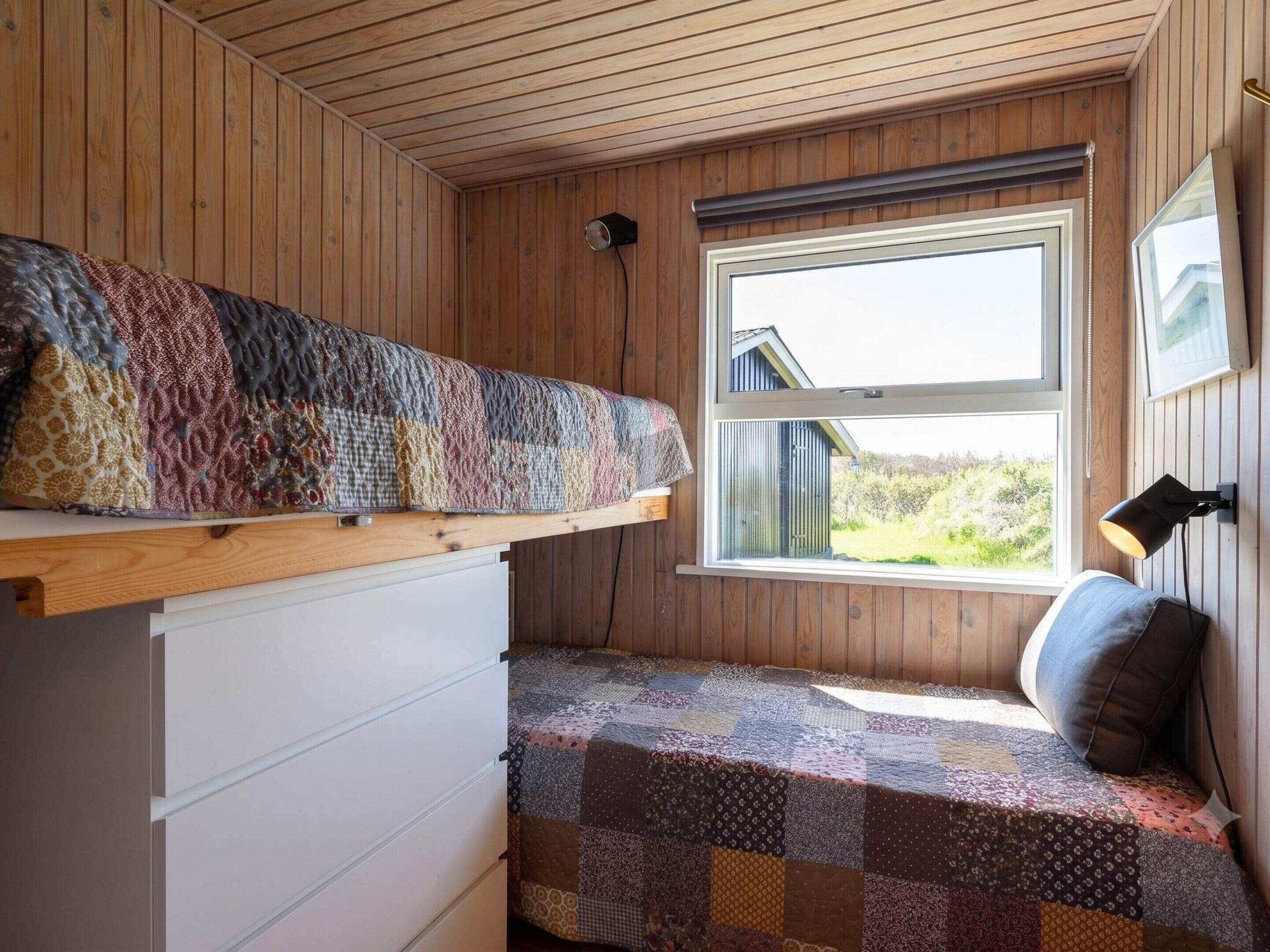 Ein kleines Zimmer mit Etagenbett, einem Fenster mit Blick, einem Schreibtisch und einem Stuhl.