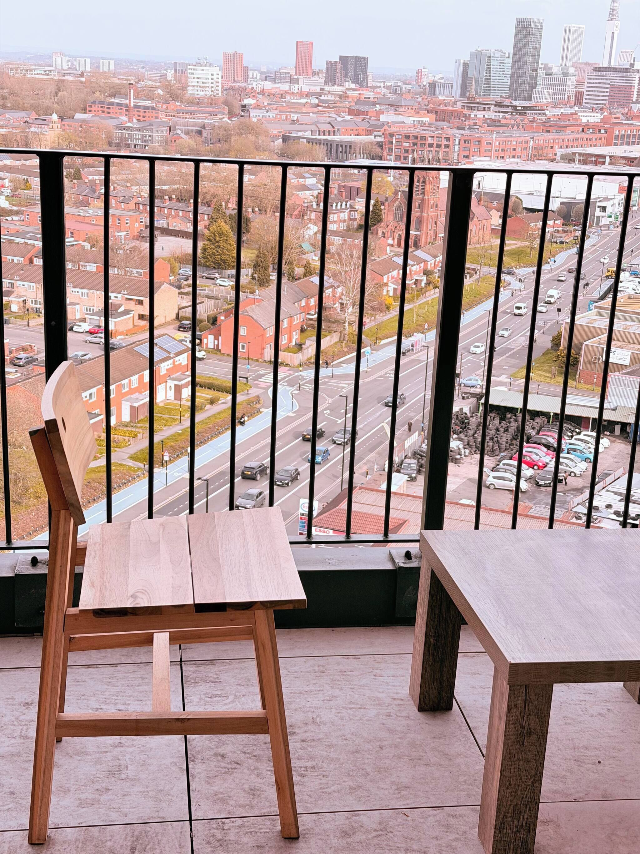 Un balcón con vistas a un paisaje urbano, una silla de madera y una mesa.