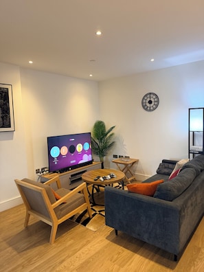 Ein modernes Wohnzimmer mit Flachbildfernseher, Spielkonsole, Sofa, Couchtisch und einer Pflanze.