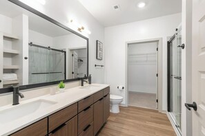 Une salle de bain moderne avec un grand miroir, deux lavabos, des toilettes et un espace douche.