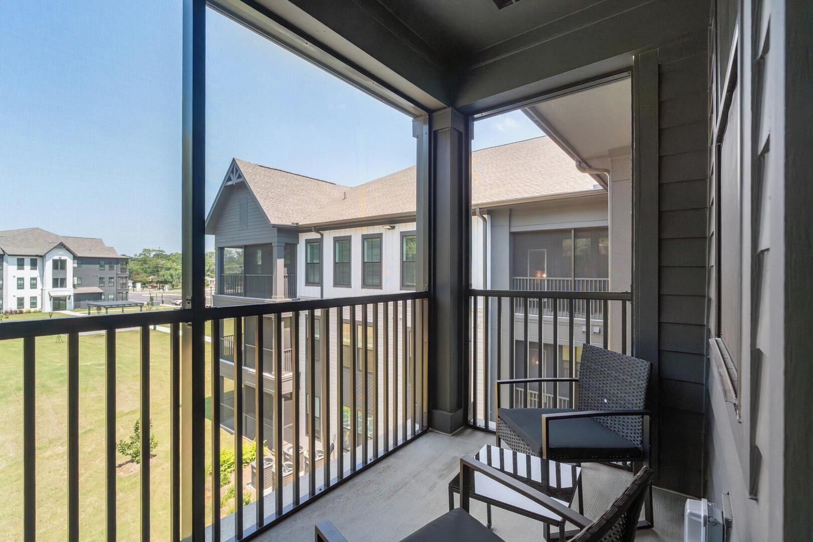 A balcony with a chair and table, overlooking a residential area with houses.