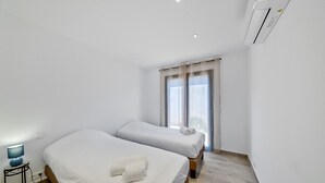 Une chambre d’hôtel avec deux lits, une table de chevet avec une lampe, une fenêtre avec des rideaux et un appareil de climatisation.