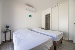Una habitación con dos camas, una mesita de noche con lámpara, un armario y un aire acondicionado.