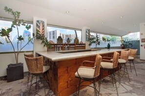 A bar area with a wooden counter and wicker chairs, large windows with city views, and indoor plants. - Luana Waikiki Studio with City Views (Honolulu)