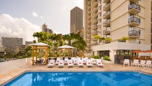 Una piscina con sillas de descanso y un pabellón, rodeada de edificios altos.