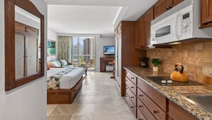 Una habitación de hotel moderna con cama, kitchenette, televisión y vistas a la ciudad.