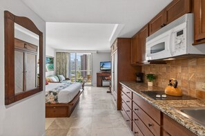 A modern hotel room with a bed, a kitchenette, a TV, and a view of the city. - Luana Waikiki Studio with City Views (Honolulu)