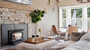 Una sala de estar acogedora con una chimenea de piedra, un comedor con mesa y sillas, y un ventanal con vistas a árboles.