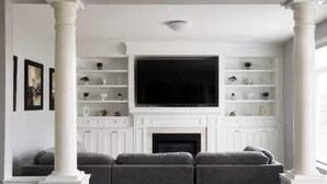 A living room with a large flat-screen TV, white cabinetry, a fireplace, and a sofa. - Spacious Getaway Stay w/ 4BR & 3BA| Niagara Falls (Welland)