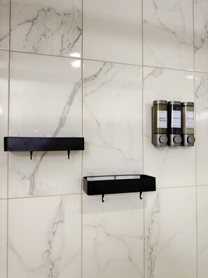 A bathroom with white marble tiles, black towel racks, and three containers labeled 'BODY WASH,' 'SHAMPOO,' and 'CONDITIONER.' -     Urban Studio Oasis (Edmonton)