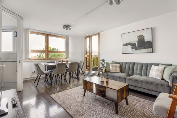 A spacious living area with a sofa, coffee table, and dining table. - Chelsea Riverside 4-Bed · Sleeps 10 · Workspace (Greater London)