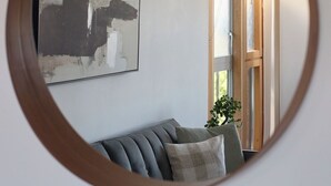 A round mirror reflecting a living room with a sofa, a painting, and a wooden door. - Chelsea Riverside 4-Bed · Sleeps 10 · Workspace (Greater London)