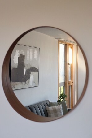 A round mirror reflecting a living room with a sofa, a painting, and a wooden door. - Chelsea Riverside 4-Bed · Sleeps 10 · Workspace (Greater London)