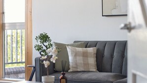 A living room with a grey sofa, a wooden coffee table, a potted plant, and a framed artwork on the wall. - Chelsea Riverside 4-Bed · Sleeps 10 · Workspace (Greater London)