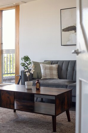 A living room with a grey sofa, a wooden coffee table, a potted plant, and a framed artwork on the wall. - Chelsea Riverside 4-Bed · Sleeps 10 · Workspace (Greater London)