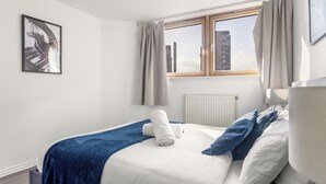 A bedroom with a bed, a window with curtains, a radiator, and a framed picture on the wall. - Chelsea Riverside 4-Bed · Sleeps 10 · Workspace (Greater London)