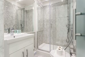Ein modernes Badezimmer mit einer Duschkabine, einem weißen Waschbecken und einem großen Spiegel.