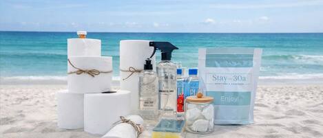 Escena de playa con artículos de aseo, una toalla y una bolsa con la etiqueta 'Stay on 30a' sobre la arena.