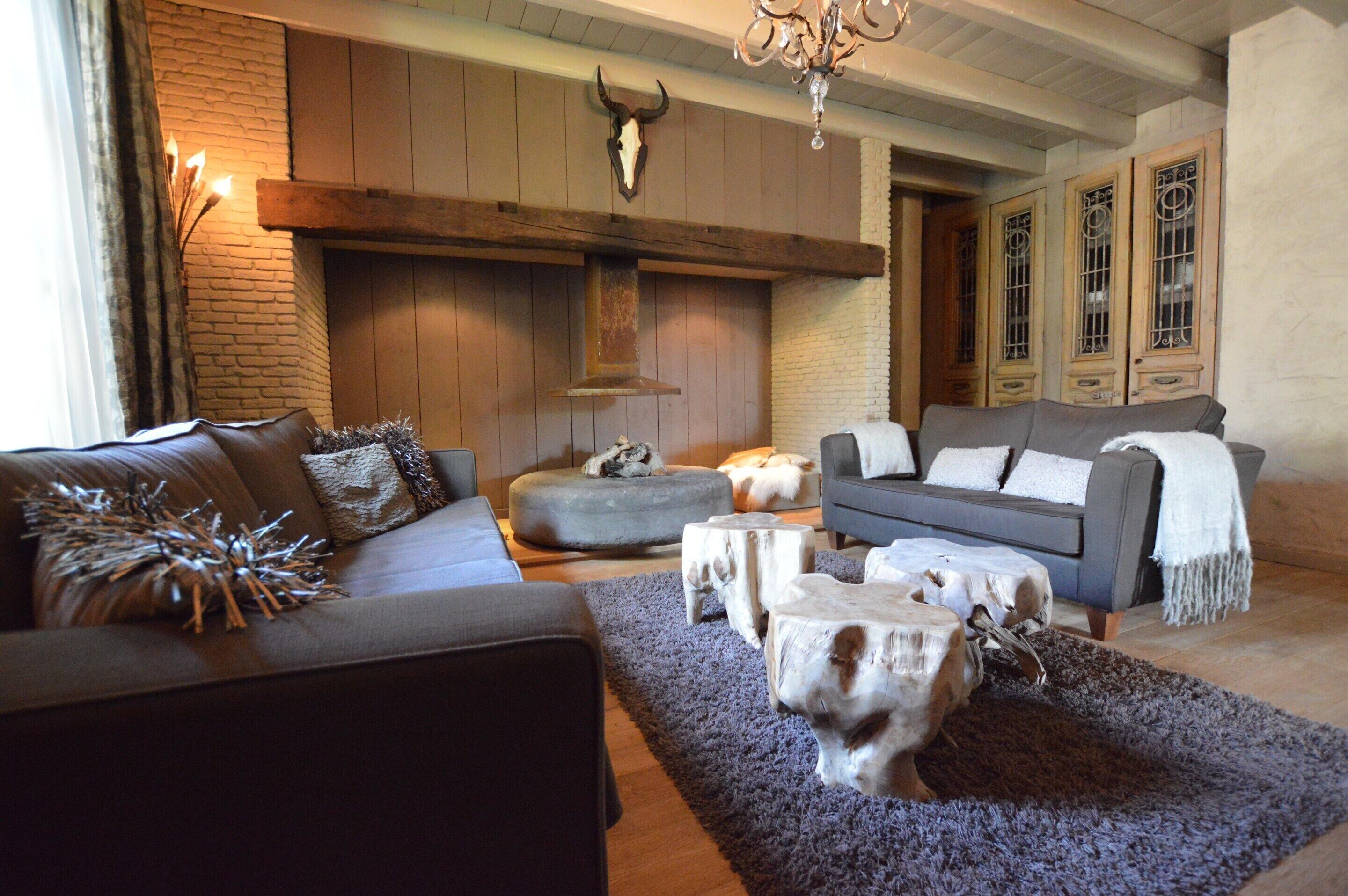 A cozy living room with a fireplace, a sofa, ottomans, and a chandelier.