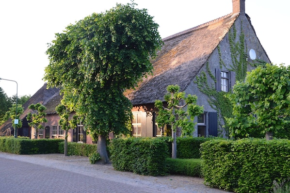 A traditional thatched-roof house with ivy-covered walls, a paved driveway, and neatly trimmed hedges. - Alphen Retreat With Sauna (Alphen)