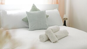 A neatly made bed with pillows and rolled towels, a bedside table with a lamp, and a window with curtains. - Cozy Flat Near Station and Local Parks (London)