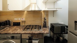 A modern kitchen with a gas stove, coffee maker, toaster, and a washing machine. - Cozy Flat Near Station and Local Parks (London)