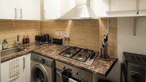 A kitchen with a gas stove, a washing machine, and a coffee machine. - Cozy Flat Near Station and Local Parks (London)