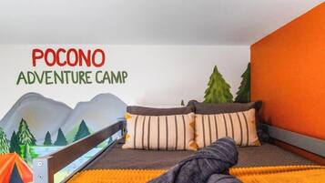 Un dormitorio con cama, almohadas, una manta, decoración tipo tienda de campaña y un mural en la pared.