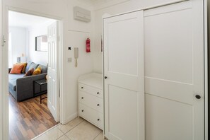Ein Flur mit grauem Sofa, weißem Kleiderschrank und einem Feuerlöscher.