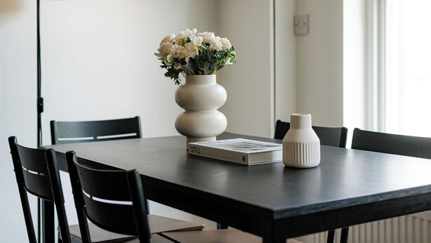 Et spisebord med en hvid vase med blomster, en bog med titlen 'STILL' og en hvid vase.