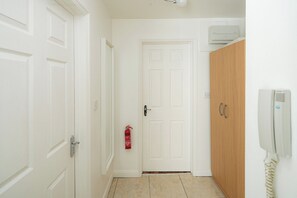 A hallway with white doors, a fire extinguisher, a wooden wardrobe, and a wall-mounted phone. - Bright Flat Near Parks and Restaurants (London)