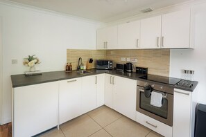 A kitchen with white cabinets, a black countertop, a microwave, a coffee maker, and a kettle. - Bright Flat Near Parks and Restaurants (London)