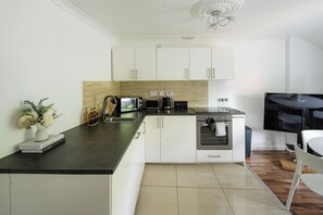 A modern kitchen with white cabinets, a black countertop, a built-in oven, a coffee maker, and a flat-screen TV. - Bright Flat Near Parks and Restaurants (London)