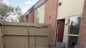 Une terrasse avec un sol en béton, une clôture en bois et deux chaises en métal.