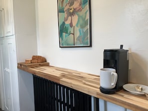 Una encimera de cocina con una cafetera, una taza blanca y un plato con una cuchara.
