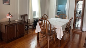 A dining room with a table set for four, wooden chairs, a cabinet, a lamp, and a window with curtains.