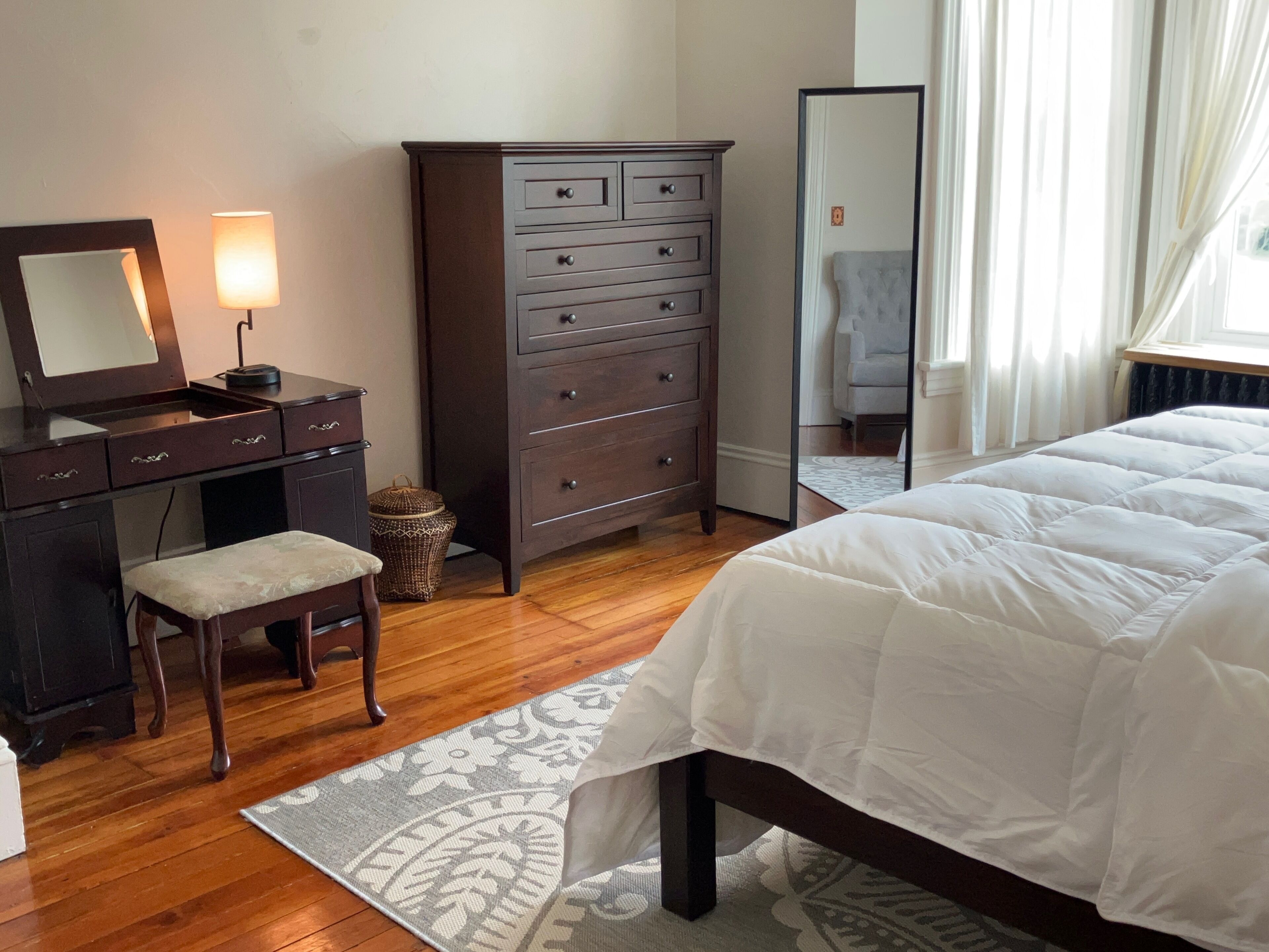 A bedroom with a bed, a dresser, a mirror, a desk, and a chair.