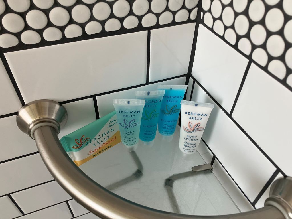 Une cabine de douche en verre avec des tubes de gel douche et de lotion pour le corps de la marque Bergman Kelly.