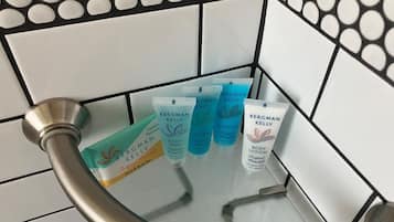 Une cabine de douche en verre avec des tubes de gel douche et de lotion pour le corps de la marque Bergman Kelly.