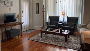 A living room with a television, two armchairs, a sofa, a coffee table, and a window with curtains.