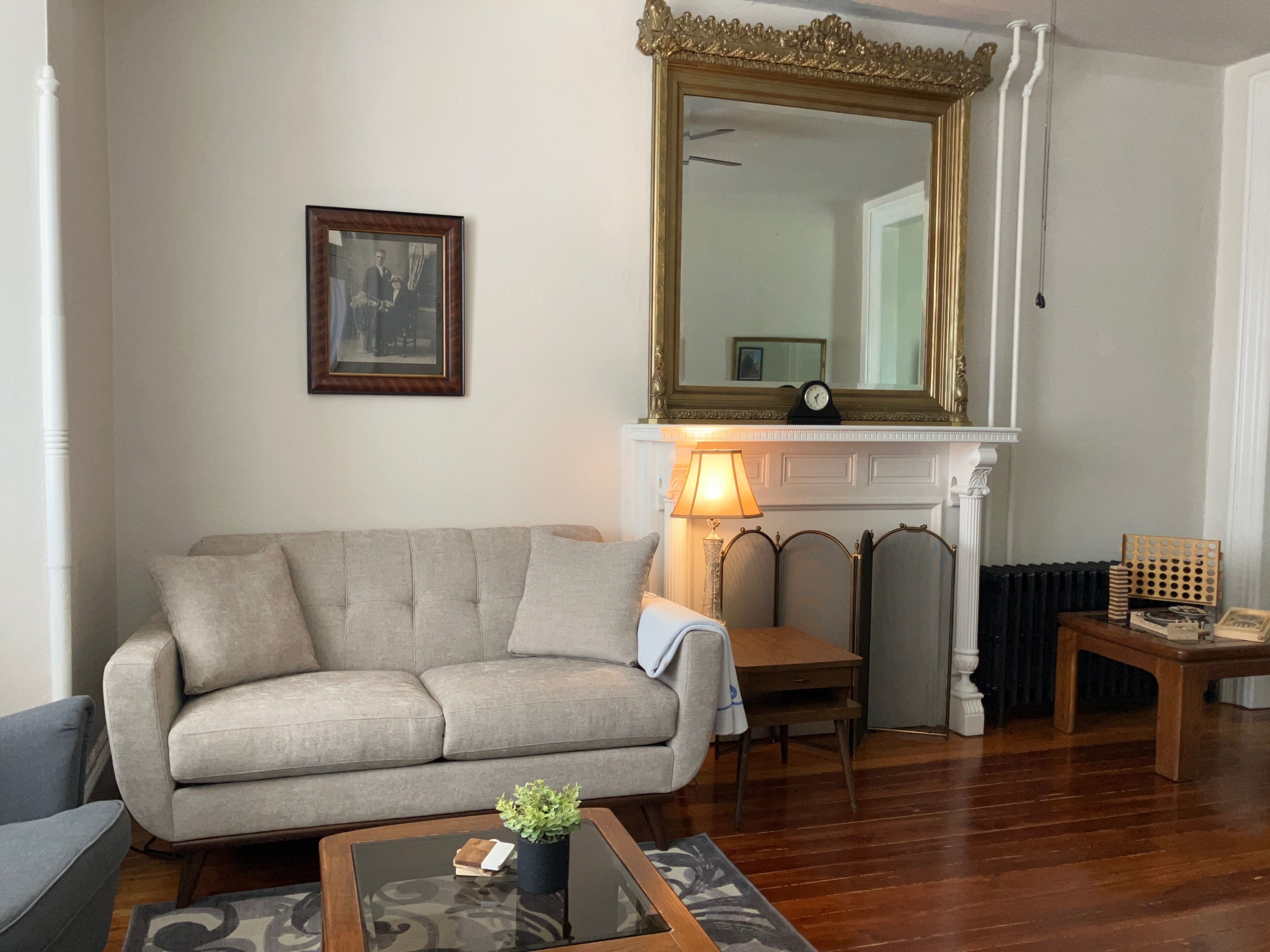 Een woonkamer met een bank, een salontafel, een lamp, een open haard en een spiegel.